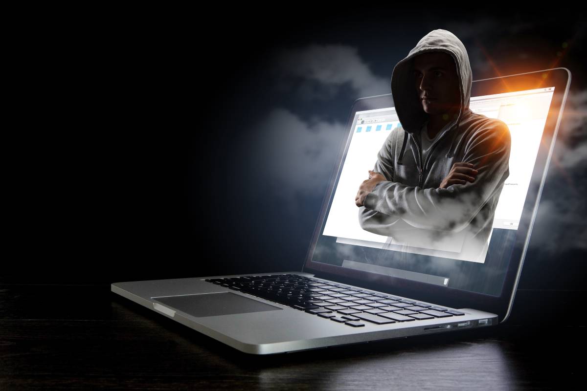 Hooded hacker stealing information on a laptop